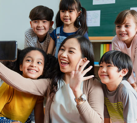 Teacher taking a cheerful selfie with a group of smiling young students, reflecting the Joyful Support and Creative & Thinking Skills (CTS) Curriculum that nurtures problem-solving, communication, and creative thinking.